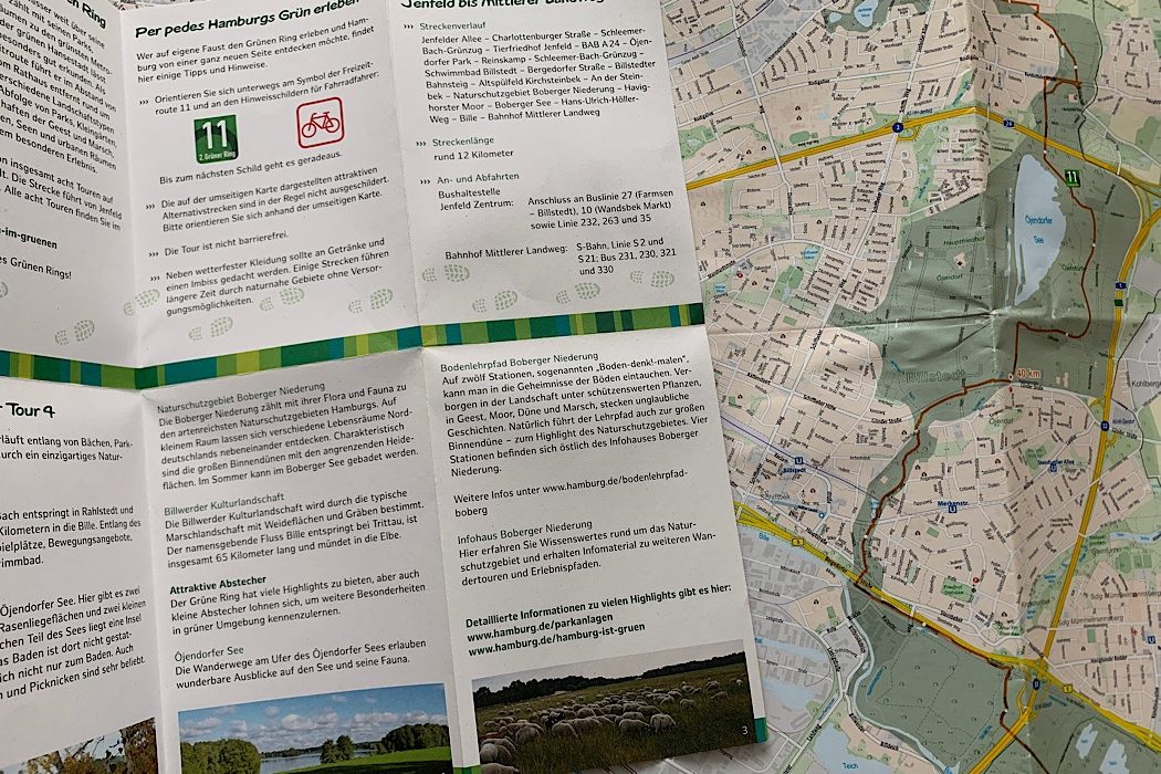 Eine Broschüre mit deutschem Text über Hamburger Radtouren liegt aufgeschlagen neben einer detaillierten Karte, die eine grüne Fahrradroute durch die Straßen und Parks der Stadt zeigt. Eine Broschüre mit deutschem Text über Hamburger Radtouren liegt aufgeschlagen neben einer detaillierten Karte, die eine grüne Fahrradroute durch die Straßen und Parks der Stadt zeigt.