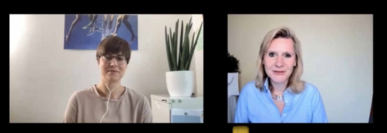 Zwei Frauen werden in einem Videogespräch mit geteiltem Bildschirm gezeigt; eine trägt eine Brille und Kopfhörer, die andere hat blonde Haare und trägt ein blaues Hemd. Im Hintergrund sind eine Pflanze und ein Kunstwerk zu sehen.