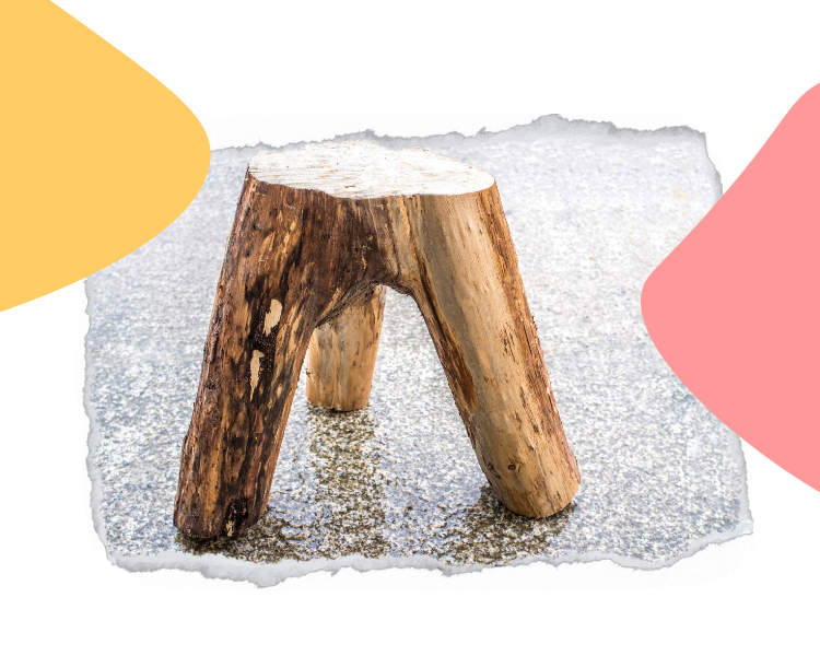 Ein dreibeiniger Holzhocker aus natürlichen Baumstämmen steht auf einer strukturierten grauen Oberfläche, mit gelben und rosa Formen im Hintergrund.